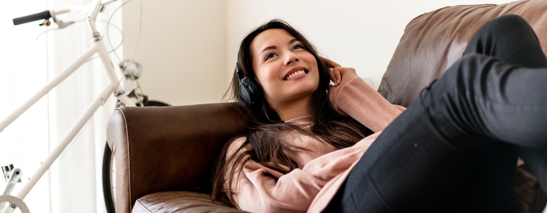 woman with headset, happily listens to music as she lays on her couch